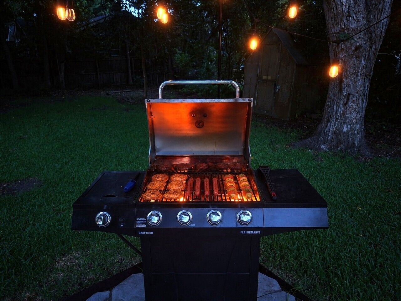 Una parrilla portátil con cuatro quemadores, un asa y una pantalla digital, colocada en un área verde al aire libre.