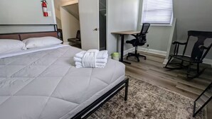Ein Schlafzimmer mit einem großen Bett, einem Schreibtisch, einem Stuhl und einem an der Wand befestigten Feuerlöscher.