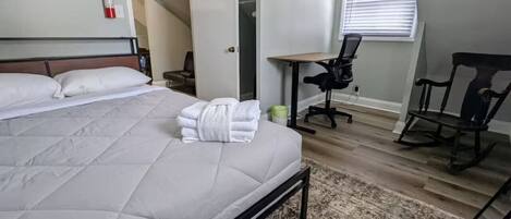 Ein Schlafzimmer mit einem großen Bett, einem Schreibtisch, einem Stuhl und einem an der Wand befestigten Feuerlöscher.