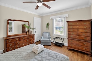 A bedroom with a bed, dresser, chair, and a ceiling fan.