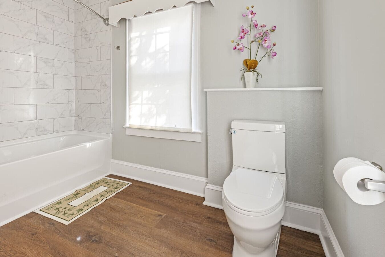 A bathroom with a bathtub, toilet, and a window with a flower vase.