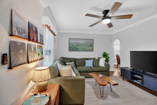 A living room with a green sofa, a wooden coffee table, a TV stand, and a ceiling fan.