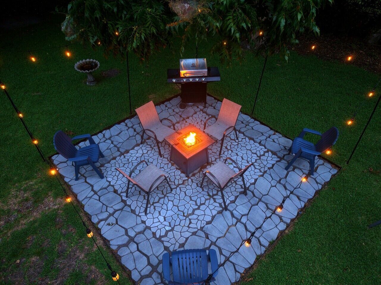 An outdoor patio with a stone floor, a fire pit, and four chairs.