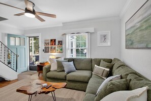 Una sala de estar con un sofá verde, una mesa de centro de madera, un ventilador de techo y una escalera.
