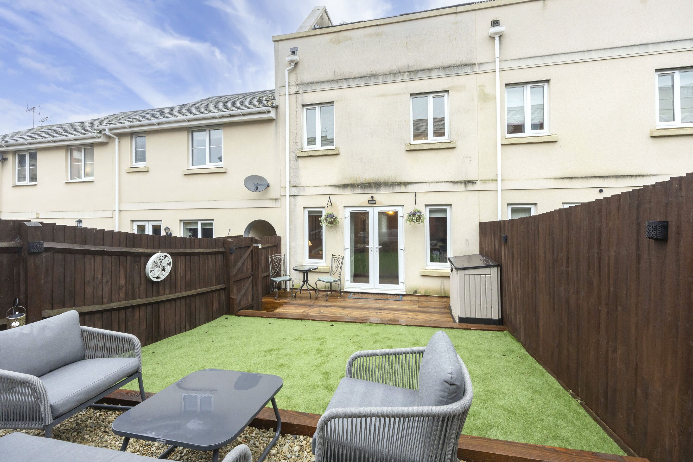 A residential building with a fenced backyard, outdoor furniture, and a small patio area.