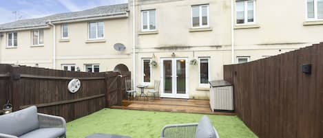 A residential building with a fenced backyard, outdoor furniture, and a small patio area.