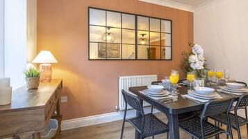 A dining area with a table set for four, a mirror on the wall, and a lamp on a side table.
