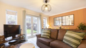 Een woonkamer met een bruine leren bank, een flatscreen-televisie, een ronde tafel en een groot raam met uitzicht op een achtertuin.