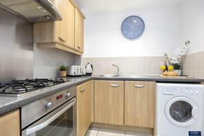 Une cuisine moderne avec des meubles en bois, un four encastré, une cuisinière à gaz, un évier et un lave-linge.