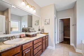 A bathroom with a large mirror, two sinks, wooden cabinets, a vanity, and a towel rack.