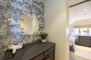 Une salle de bain avec un meuble-lavabo foncé, un miroir rond et un sèche-cheveux posé sur le comptoir.