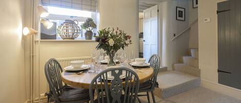 A dining area with a round table set for four, surrounded by chairs, a vase with flowers, and a pendant light.