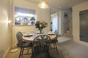 Un coin repas avec une table ronde dressée pour quatre personnes, entourée de chaises, un vase avec des fleurs et une suspension.
