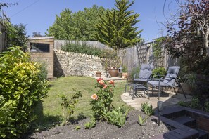 A backyard with a stone wall, a patio with chairs, and a flower bed with roses.