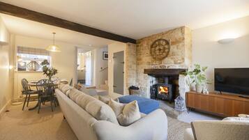 A living room with a stone fireplace, a sofa, a television, and a dining area with chairs and a table.