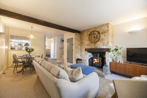 A living room with a stone fireplace, a sofa, a television, and a dining area with chairs and a table. - Charming Cotswold Cottage in Central Winchcombe (Winchcombe)