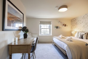 Une chambre à coucher comprenant un lit, un bureau, une chaise, une fenêtre et une étagère fixée au mur, sur laquelle sont posés des livres.