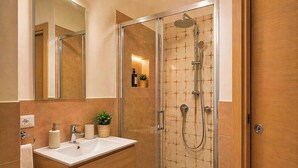 Un baño moderno con ducha envuelta en vidrio, tocador de madera y lavamanos blanco.