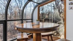 Una mesa redonda de madera con bancos dentro de una habitación con ventanas amplias.