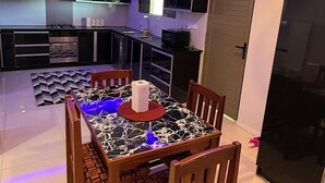 Una cocina moderna con armarios negros, horno empotrado y comedor con mesa de mármol y sillas de madera.