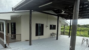 Una terraza techada al aire libre con piso de madera, estructura de pérgola y vistas a un paisaje natural.