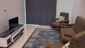 Una sala de estar con televisor de pantalla plana, sofás estampados, alfombra con diseño y un equipo de aire acondicionado.