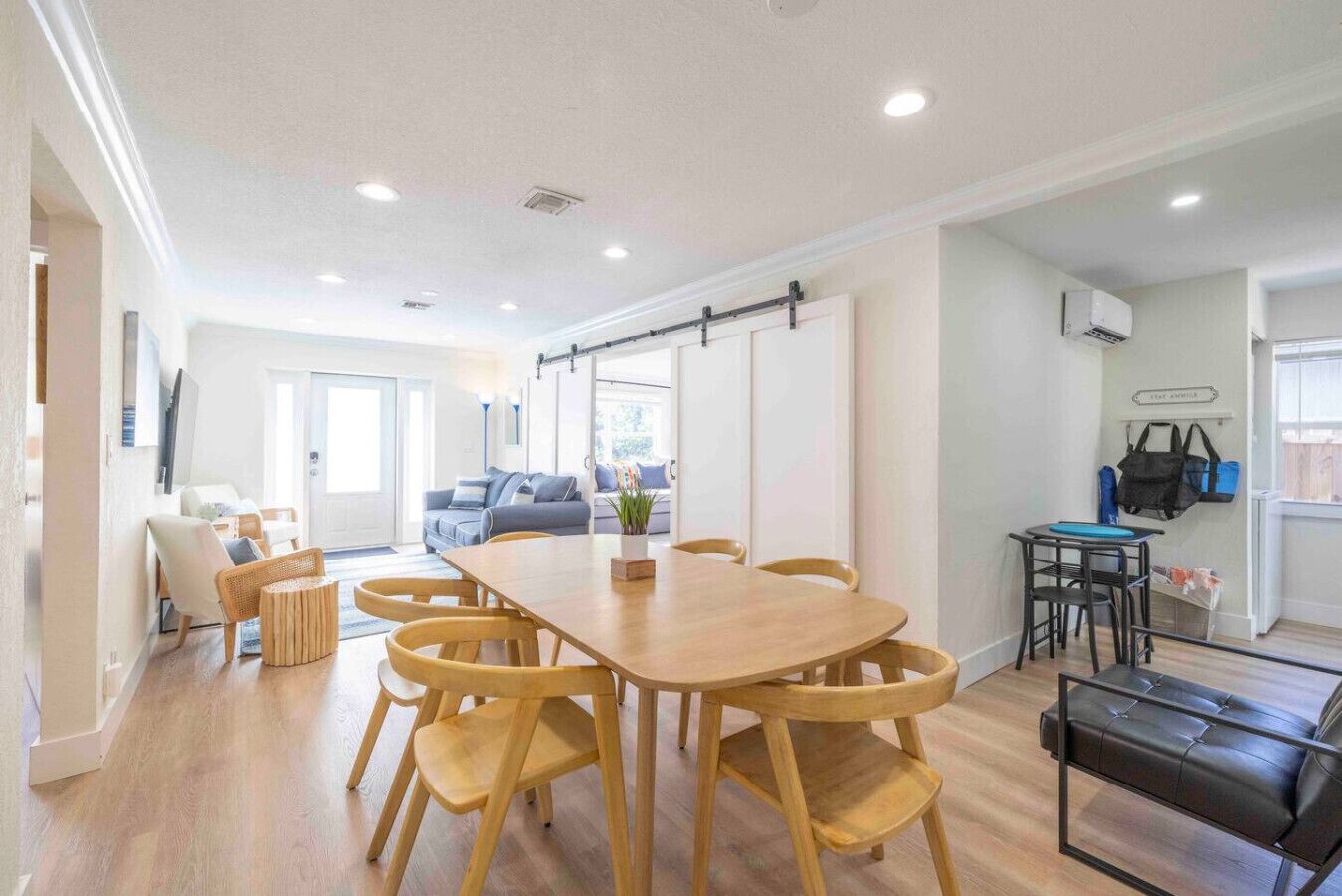 A spacious living area with a large wooden dining table surrounded by chairs, a sofa, and a small table with a chair.