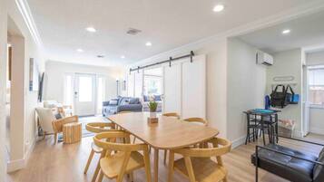 A spacious living area with a large wooden dining table surrounded by chairs, a sofa, and a small table with a chair.
