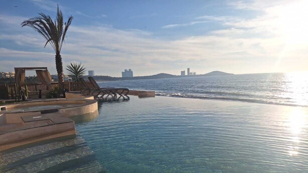 Una piscina infinita cristalina con vistas al mar y edificios lejanos.