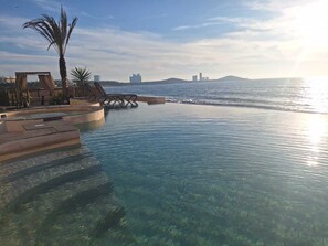 A clear infinity pool with a view of the sea and distant buildings. - Exclusive beachfront apartment! (Sin.)