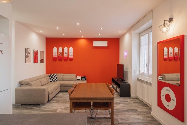 Ett modernt vardagsrum med ett matbord i trä, en beige soffa och en röd accentvägg.