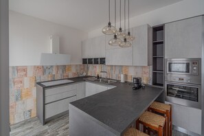 Ett modernt kök med en central köksö, rostfria vitvaror och ett mönstrat stänkskydd.