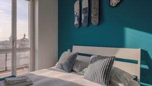 Quarto com cama, duas almofadas, uma janela e três objetos fixados na parede.