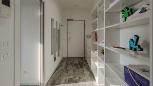 Um corredor com piso de madeira, paredes brancas e uma porta com a inscrição "DRAMATIC EXIT". Prateleiras do lado direito estão vazias.