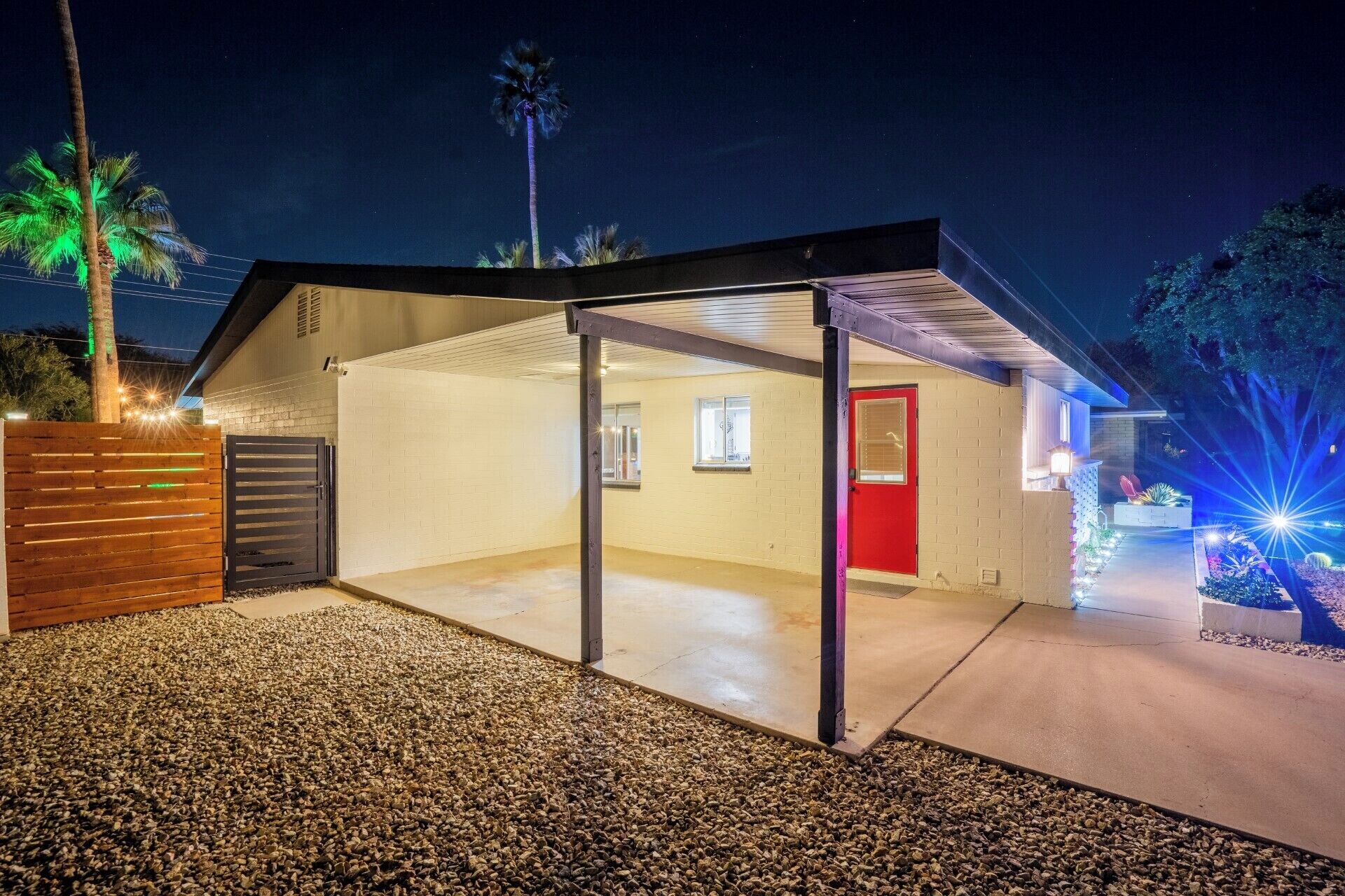 A modern house with a covered garage, a red door, and a well-lit driveway.