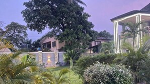 A landscaped garden with a large tree, a gazebo, and a building with a lighted entrance. - BRAVA HOTEL  (Ibadan)