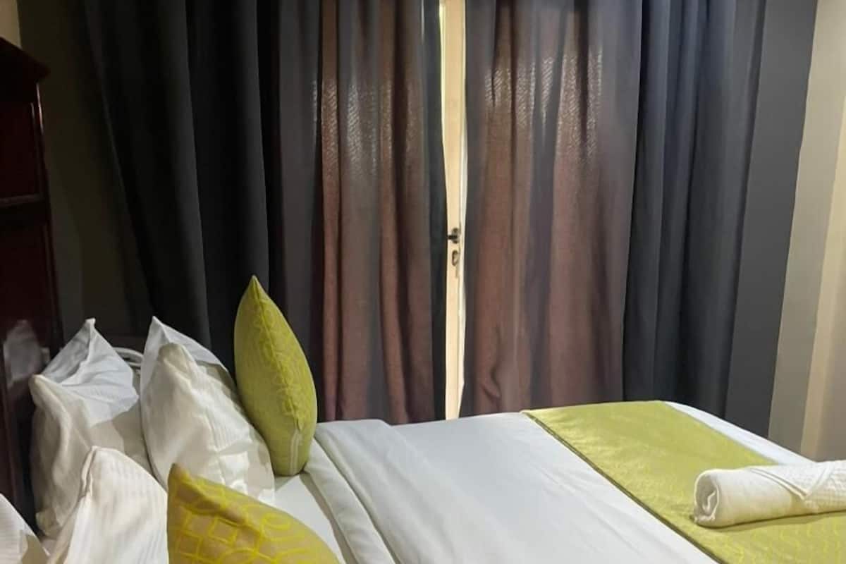 A hotel room with a bed, pillows, a window with curtains, and a door.