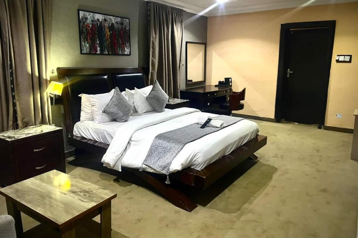 A hotel room with a bed, bedside table, lamp, and a painting on the wall.