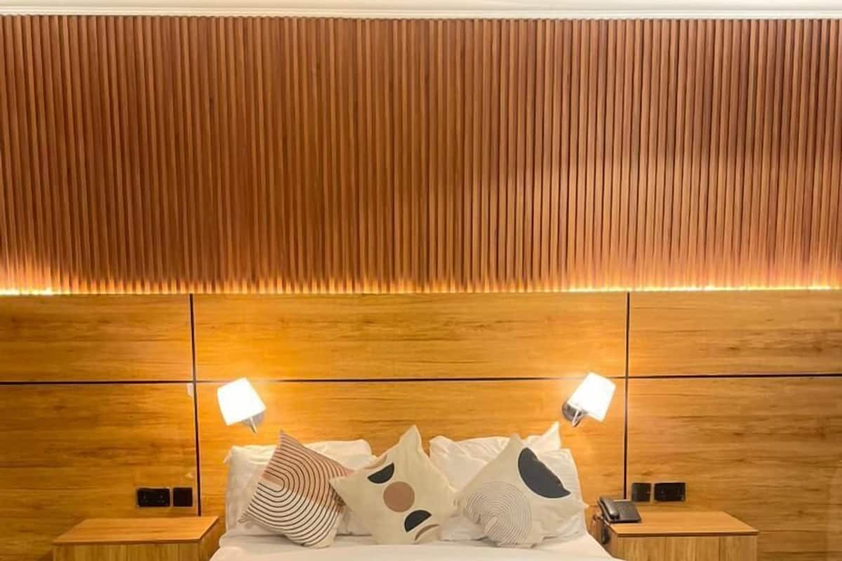 A modern bedroom with a wooden headboard, a large bed with white bedding, two bedside tables with lamps, and a textured wall behind the bed.