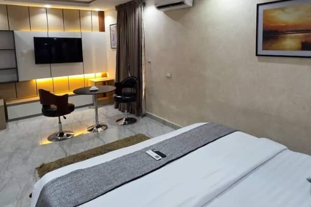 A modern hotel room with a large bed, a desk, a chair, a TV, and an air conditioning unit.