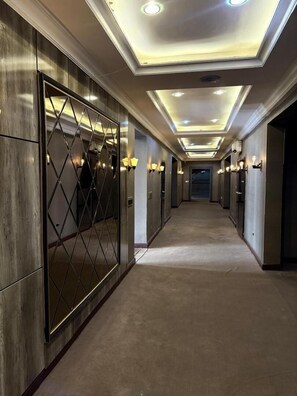 Un pasillo de hotel con un camino central, paredes espejadas e iluminación empotrada en el techo.
