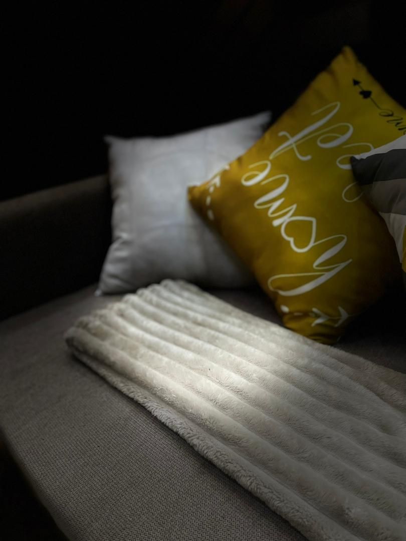 En soffa med en vit pläd och en gul kudde med vit text.