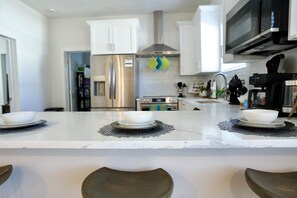 A modern kitchen with white cabinets, stainless steel appliances, and a marble countertop. - Casa De Ybor 3Bd, 2Bth, 4 beds, Historic Charm, Modern Lux (Tampa)