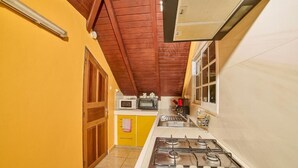 Una cocina con estufa a gas, microondas y una ventana con persianas.