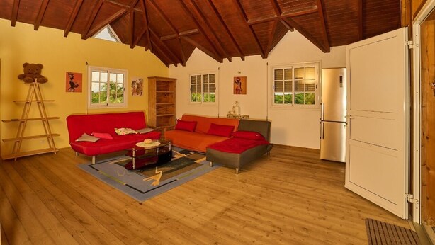 Un salón amplio con techo alto, piso de madera y un sofá rojo.