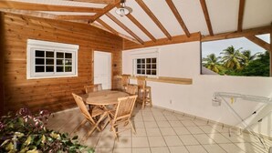 Una cabaña de madera con suelo de baldosas, una mesa de comedor con sillas y vistas a palmeras.