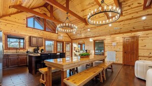 Ein großzügiges Holzblockhaus-Interieur mit einem großen Esstisch, Bänken, einer Küchenzeile und einer gemütlichen Sitzecke.