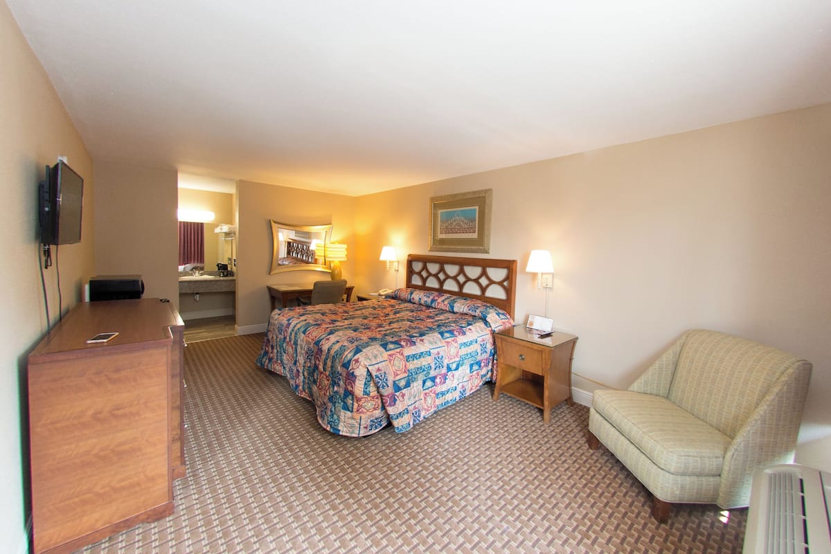 A hotel room with a bed, a desk, a chair, a TV, and a lamp.