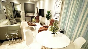 A modern living room with a dining area, featuring a round table and white chairs, a sofa, and a TV mounted on the wall. - The Villa unit - The Agustin Guesthouse for Men, a beautiful & sexy resort oasis (Fort Lauderdale)