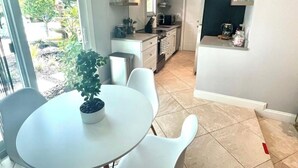 A modern kitchen with white cabinets, a dining area with a table and chairs, and a view of the outdoors through a sliding glass door. - The Villa unit - The Agustin Guesthouse for Men, a beautiful & sexy resort oasis (Fort Lauderdale)